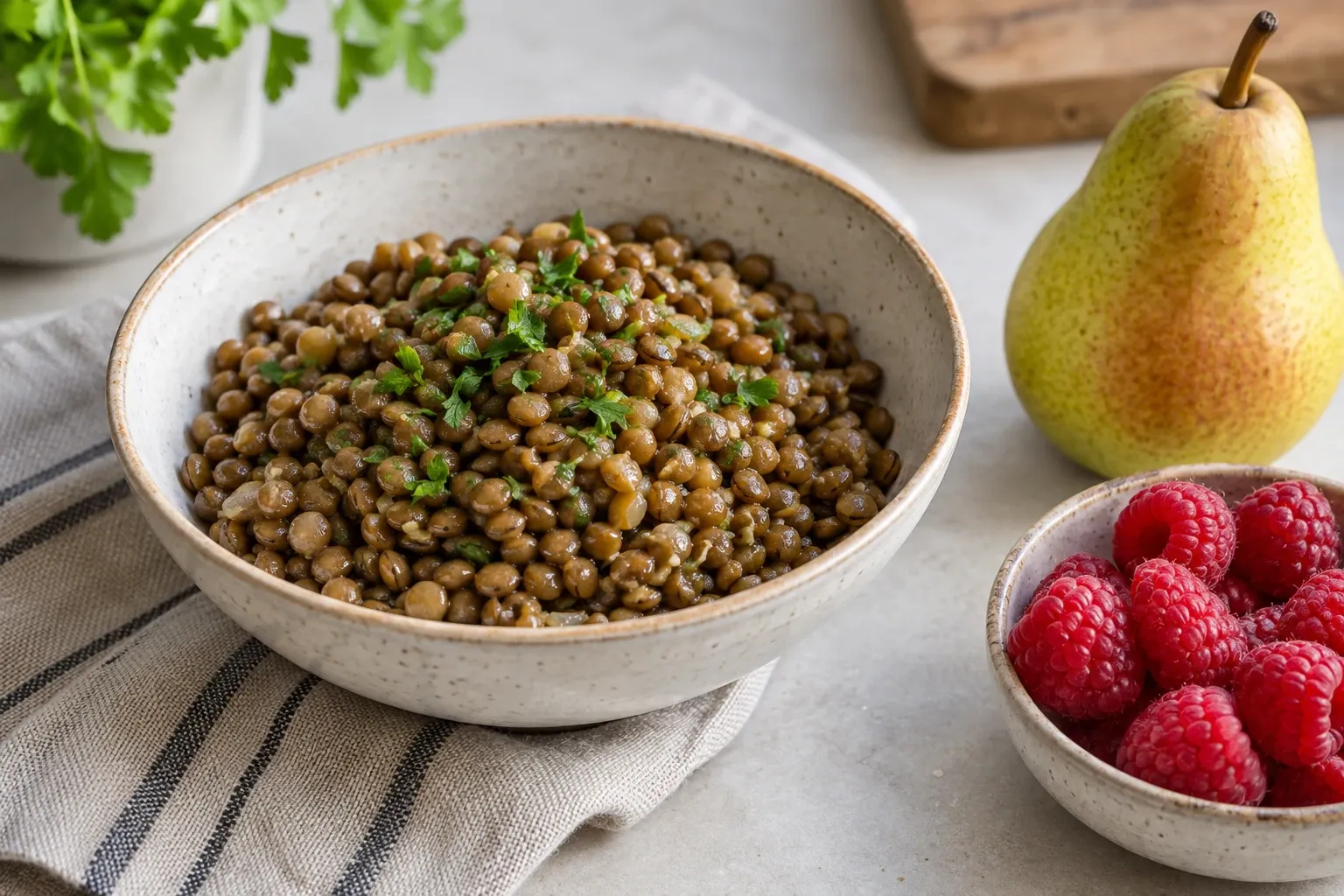 Bowl of cooked lentils garnished with parsley beside raspberries and a pear