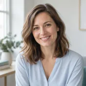 Smiling woman with shoulder-length brown hair in a light blue blouse, photographed in soft daylight